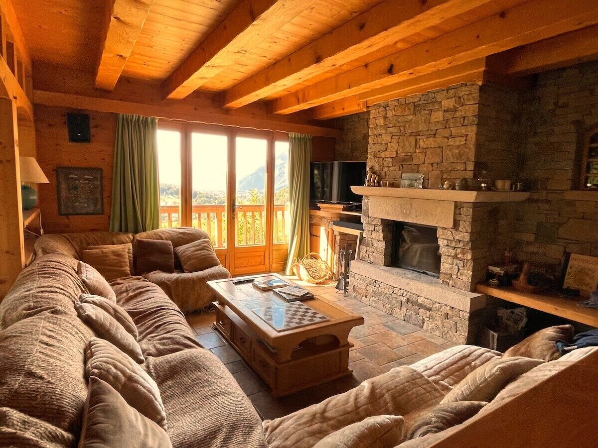 A cozy living room with a stone fireplace, wooden beams, and a large window overlooking a scenic view.