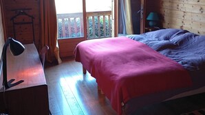 A wooden cabin room with a bed, a desk with a lamp, a chair, and a window with curtains. - 10 min from Lake Annecy, large, quiet chalet with view (Faverges-Seythenex)