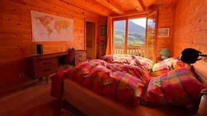 A cozy cabin room with a wooden interior, a bed with colorful bedding, a desk with a chair, a map on the wall, and a window with a view of a mountain landscape. - 10 min from Lake Annecy, large, quiet chalet with view (Faverges-Seythenex)
