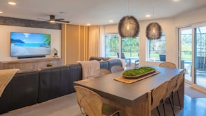 A modern living room with a large flat-screen TV, a wooden dining table, and a cozy seating area.