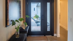 A modern entrance with a black door, a potted plant, and a framed artwork on the wall.