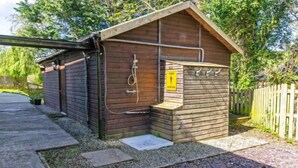 A wooden cabin with a small porch, a hose for water, and a yellow sign indicating a private area. - Streamways Slps 12-16 Hot Tub with Views & Cabin (Croyde)