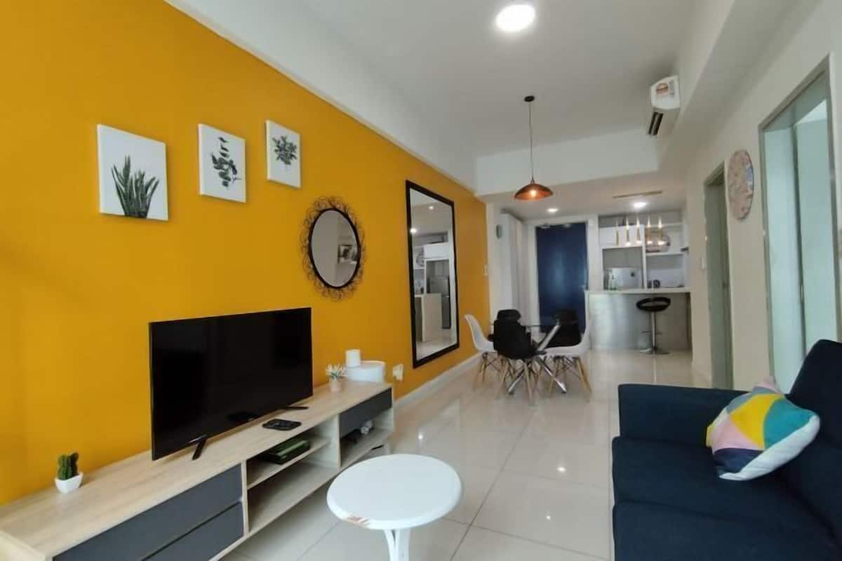 Een moderne woonkamer met een grote flatscreen-tv, een eethoek met een tafel en stoelen, en een keuken op de achtergrond.
