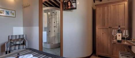 Een hotelkamer met een bed, een douche, een houten kledingkast en een klein tafeltje met glazen en een fles.