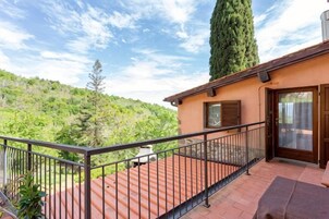 Uma varanda com grade de metal, uma porta com janela e vista para um morro com árvores.