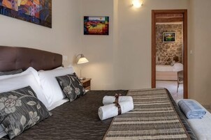 Quarto de hotel com uma cama grande, uma mesa de cabeceira com luminária, uma pequena mesa com uma cadeira e um quadro na parede.