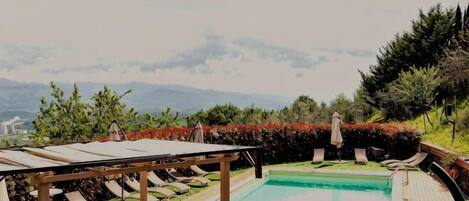 Zona de piscina con sillones reclinables, una pérgola y vistas a montañas.