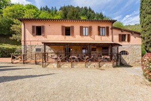 A two-story building with a stone foundation, wooden balcony, and a gravel driveway. - Private Country House with swimming pool -Chianti (Cavriglia)