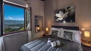 Ein Schlafzimmer mit großem Fenster, einem Bett mit gestreifter Bettwäsche, einem Blumenbild und Nachttischlampen.
