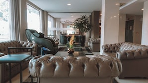 Eine moderne Hotelhalle mit Ledersofas, einem Massagesessel und einer Rezeption.