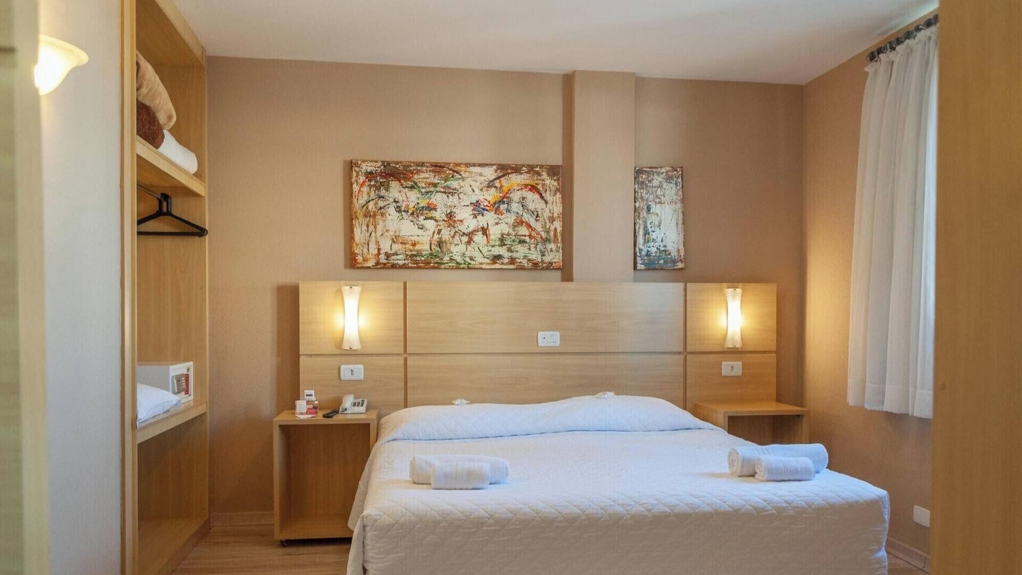 Una camera d'albergo con un letto grande, comodini, un armadio e due quadri appesi al muro.