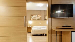 Une chambre d’hôtel moderne avec un plancher en bois, un lit avec une literie blanche, une table de chevet avec une lampe et un téléviseur à écran plat fixé au mur.