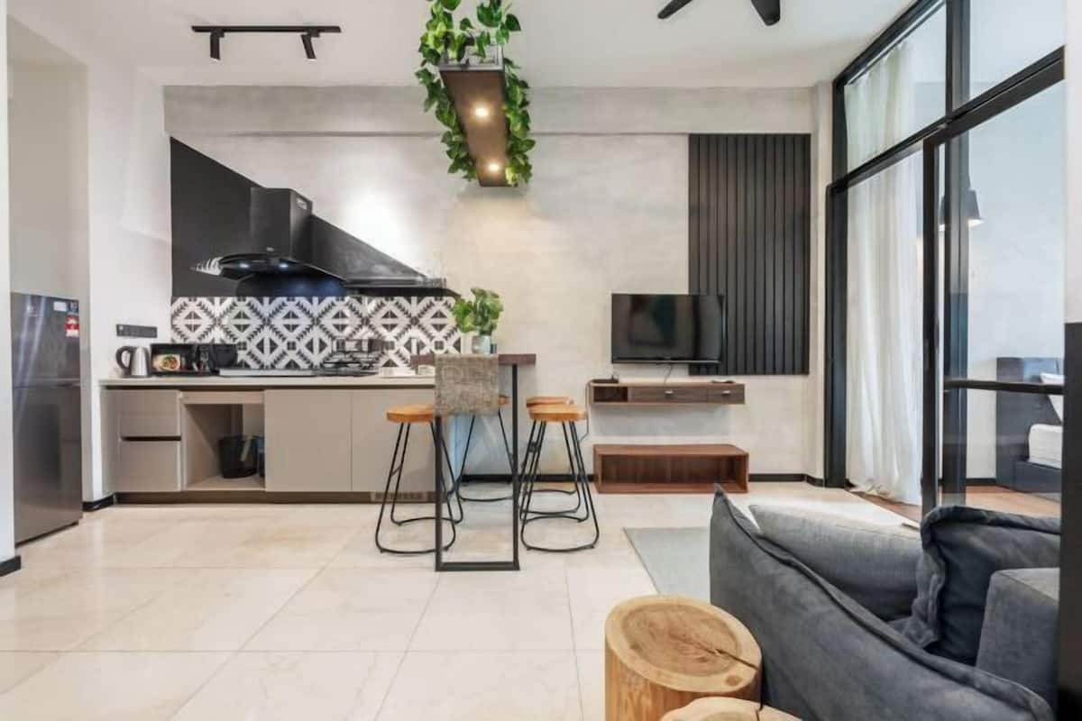 A modern kitchen with a central island, bar stools, a TV, and a large window.