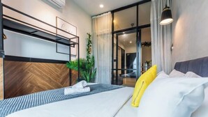 Een moderne hotelkamer met een bed, een bureau met stoel, een kamerplant en een glazen schuifdeur die leidt naar een balkon.