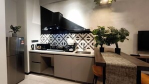 Een moderne keuken met een ingebouwde kookplaat, een magnetron en een koffiezetapparaat. Er staat een eettafel met een stoel en een potplant.