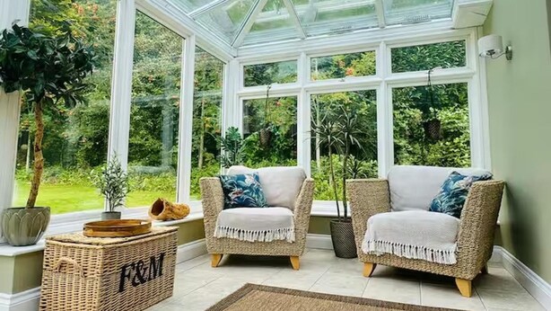 Une véranda meublée de mobilier en osier, avec une grande plante et un panier portant l’inscription « F&M ».