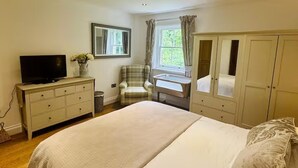 Une chambre à coucher avec un lit, un téléviseur posé sur une commode, une chaise, une fenêtre avec des rideaux et une armoire.