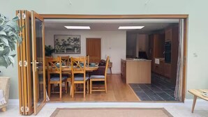Une pièce dotée d’une porte coulissante qui donne sur un coin repas avec des meubles en bois et une cuisine au carrelage foncé.
