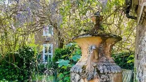 Une grande urne décorative dans un jardin, avec des fleurs violettes et un bâtiment en briques en arrière-plan.