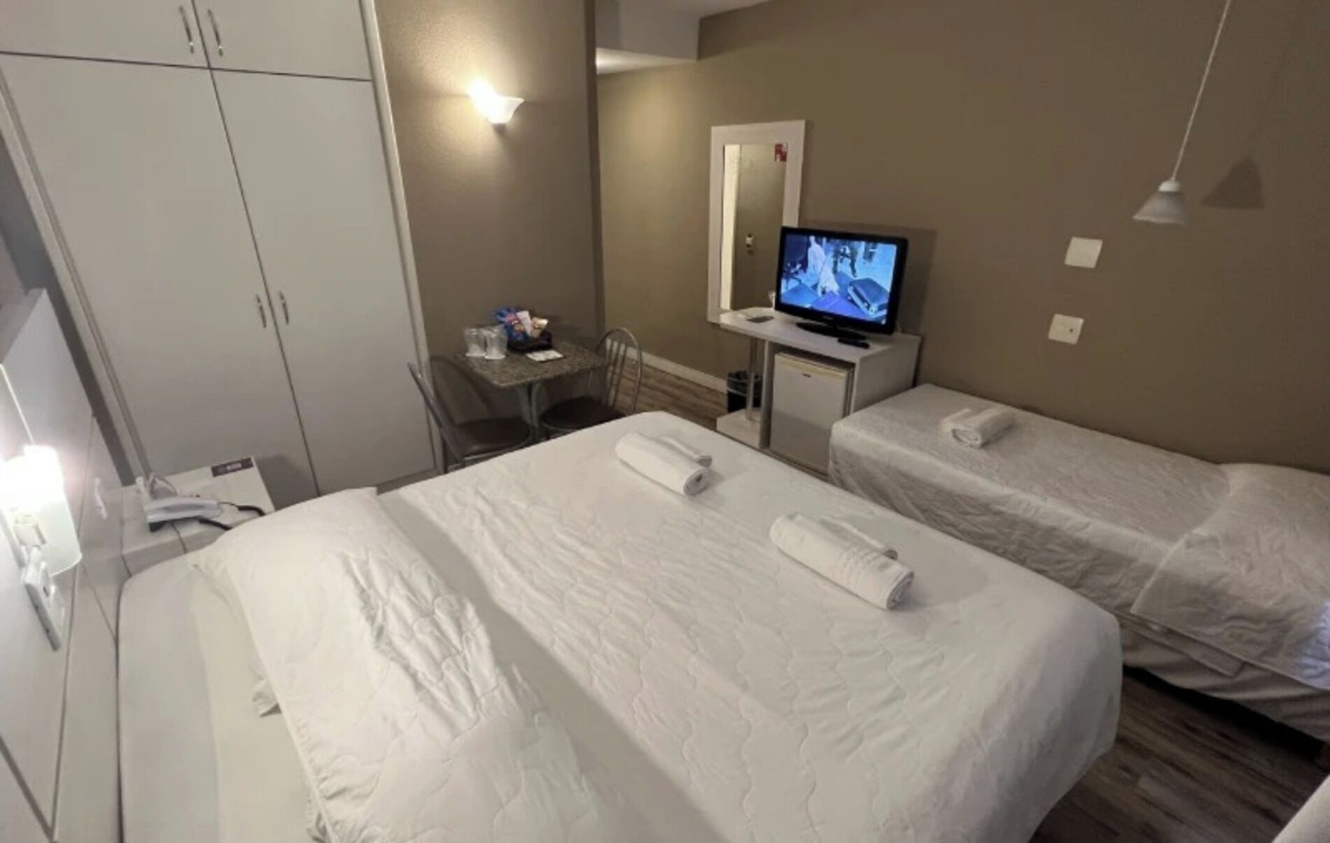 A hotel room with two beds, a desk with a computer, a television, and a wardrobe.