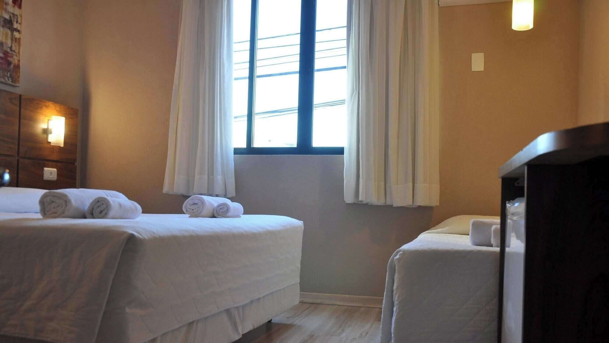 Une chambre d’hôtel avec deux lits, un bureau et une fenêtre avec des rideaux.