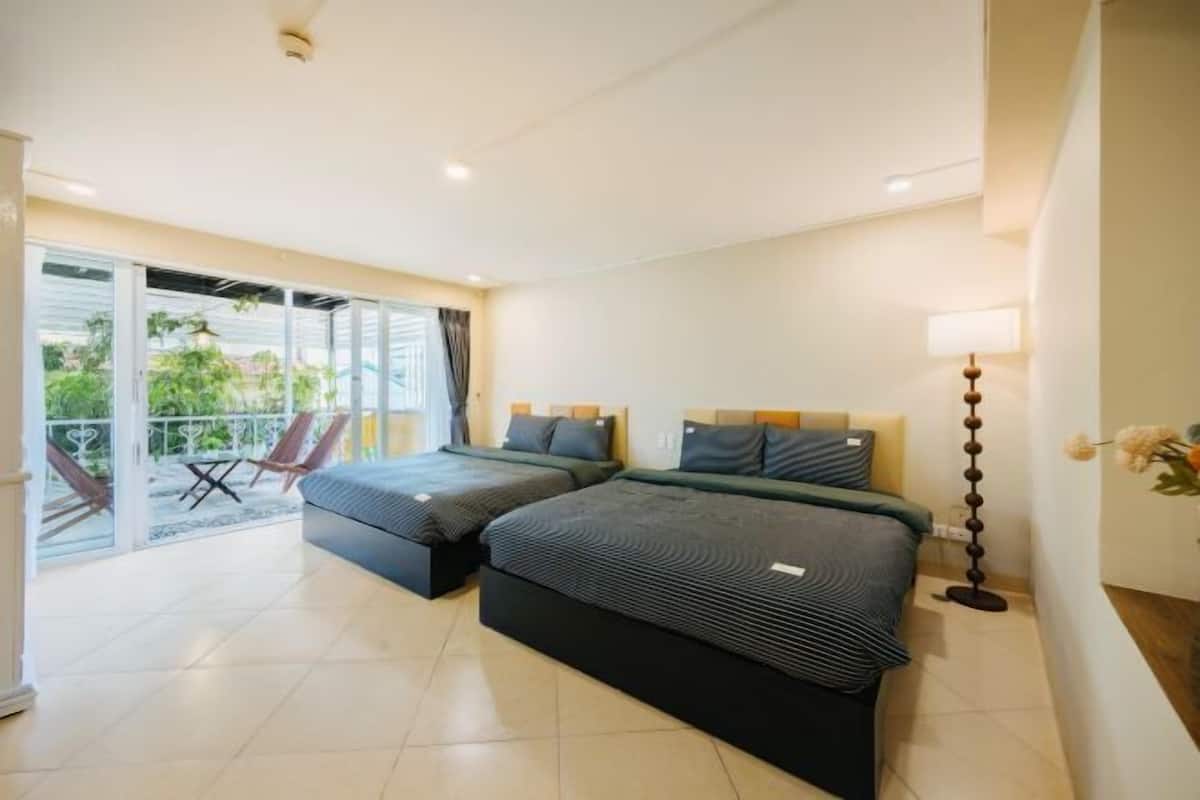 A hotel room with two beds, a balcony with chairs, and a lamp.