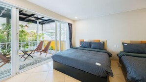A bedroom with two beds, a sliding glass door leading to a balcony, and a small table with chairs. - VietHOME - 22 Pho Hue - Duplex 67 (Hanoi)