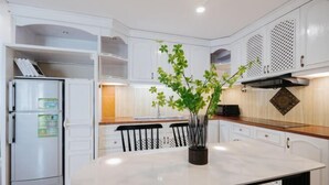 A modern kitchen with white cabinetry, a marble countertop, and a central island with a potted plant. - VietHOME - 22 Pho Hue - Duplex 67 (Hanoi)