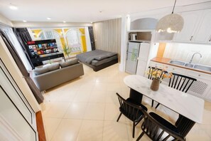 A modern living room with a sofa, a dining table with chairs, and a kitchen area with cabinets and a sink. - VietHOME - 22 Pho Hue - Duplex 67 (Hanoi)