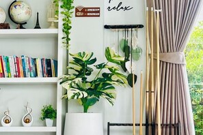 A room with a bookshelf, a potted plant, a hanging plant, and a curtain. - Relax Pool Villa Khaoyai (Pak Chong)