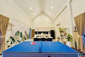 A ping pong table in a room with a high ceiling and a kitchen in the background. - Relax Pool Villa Khaoyai (Pak Chong)