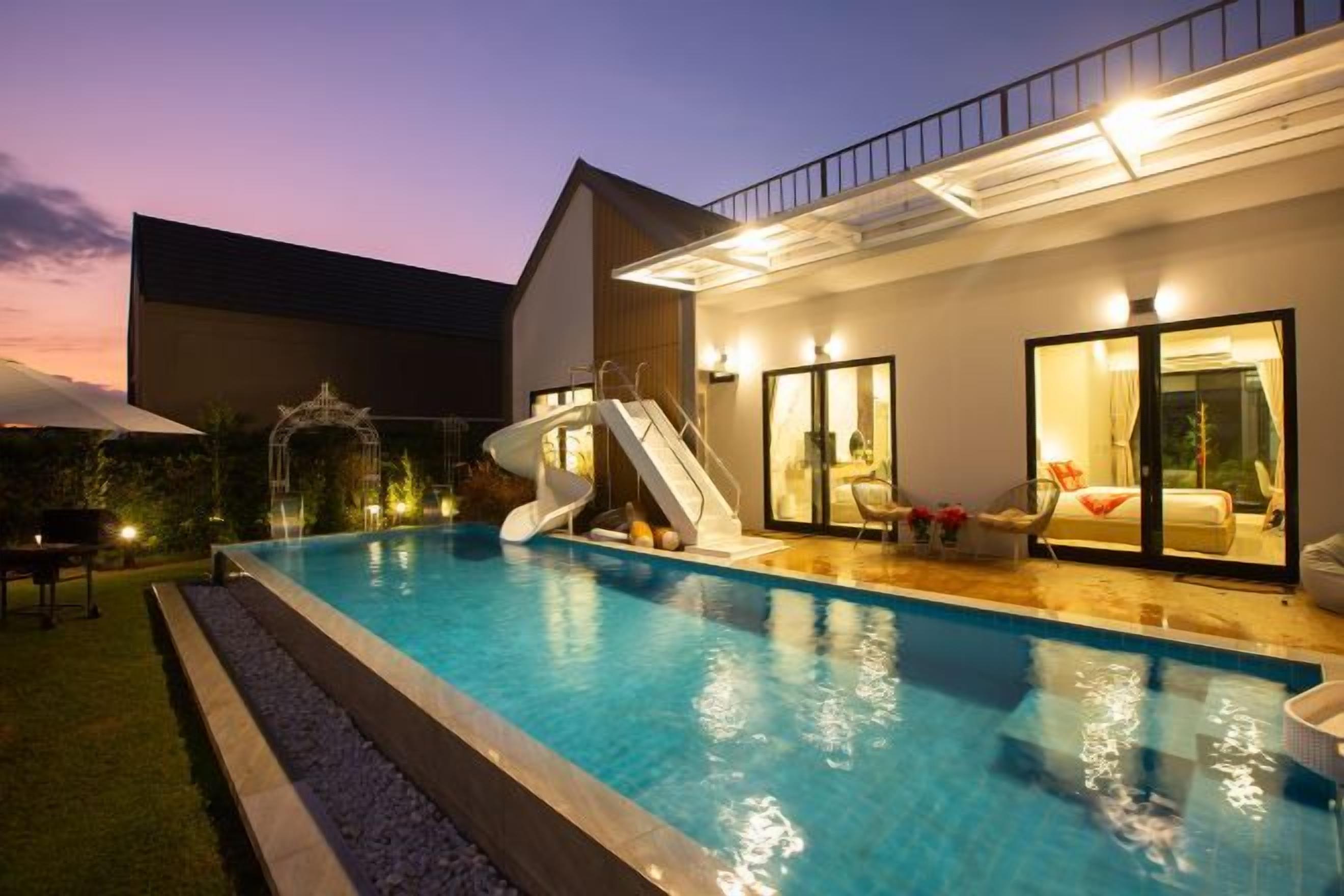 A swimming pool with a slide, a covered seating area, and a building with glass doors.