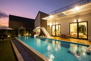 A swimming pool with a slide, a covered seating area, and a building with glass doors. - Relax Pool Villa Khaoyai (Pak Chong)