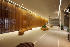 Un moderno vestíbulo de hotel con un mostrador de recepción de madera, zonas de estar y un gran cartel que dice 'CENTURA'.