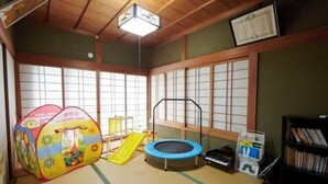 Um espaço com tatames, área de recreação com escorrega e trampolim, estante e um certificado na parede.