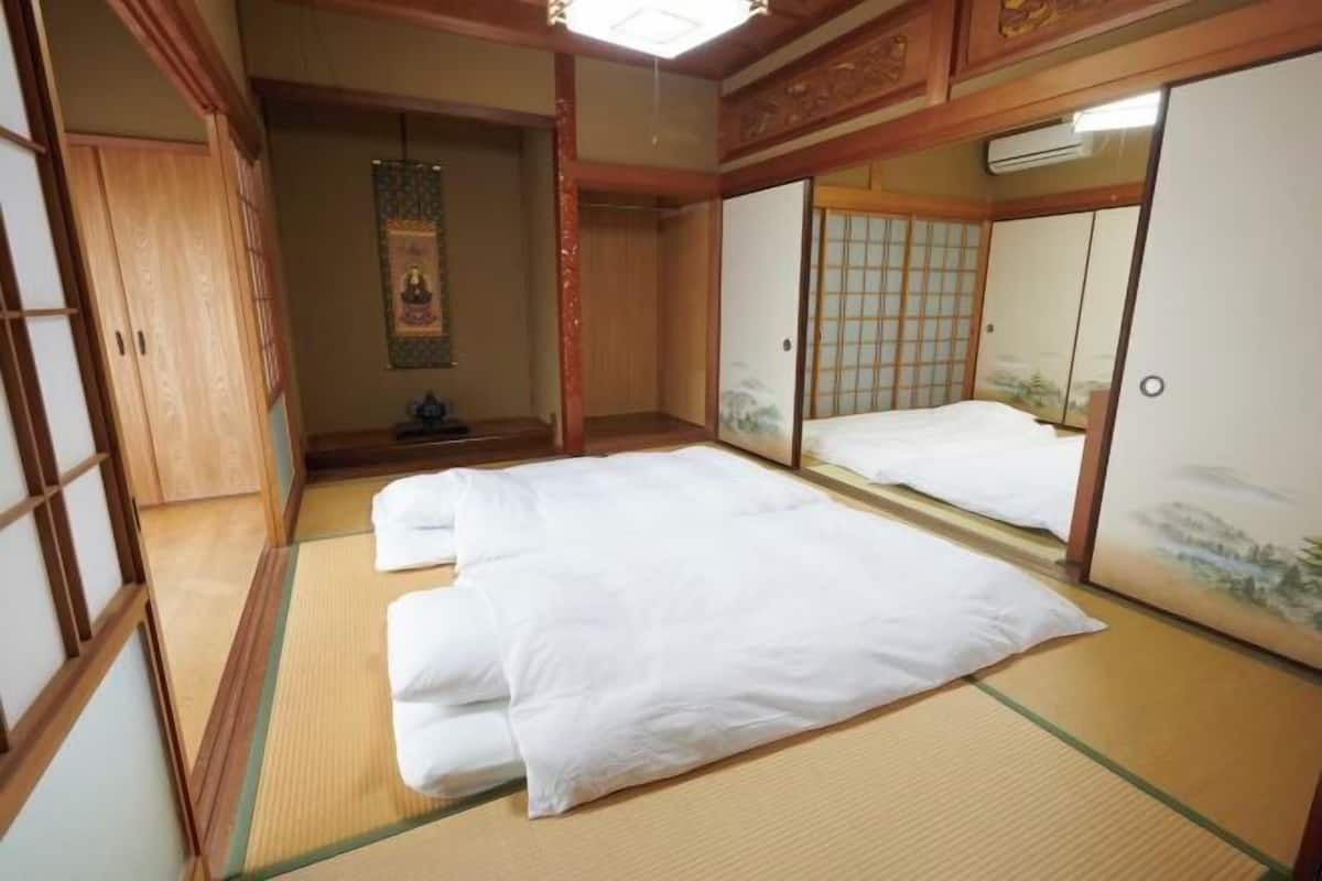 Une pièce de style japonais traditionnel, avec un sol recouvert de tatamis, un futon servant de lit, des portes coulissantes et un rouleau calligraphique suspendu.