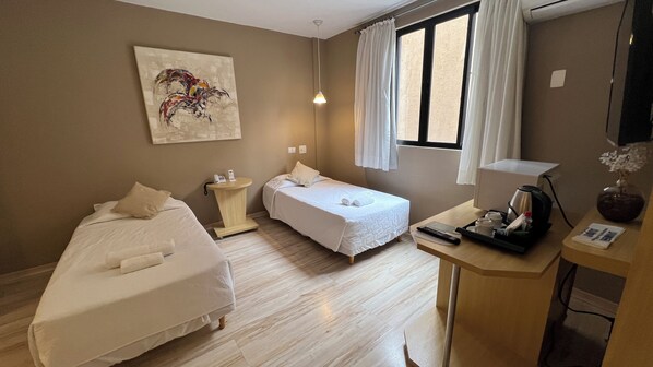 A hotel room with two beds, a small table with a coffee maker, a painting on the wall, and a window with curtains. - Two Downtown Executive Double Twin Room for Relaxing Stays and Urban Exploration (Paraná)