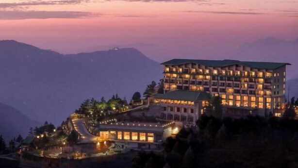 A multi-story hotel with a prominent green roof, situated on a hillside with a view of surrounding mountains. - dusitD2 Fagu (Shimla)