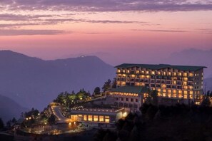 A multi-story hotel with a prominent green roof, situated on a hillside with a view of surrounding mountains. - dusitD2 Fagu (Shimla)