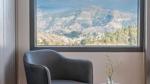 A room with a large window, a black chair, and a small table with a vase. - dusitD2 Fagu (Shimla)