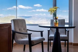 A room with a large window, two chairs, a table, and a vase with flowers.