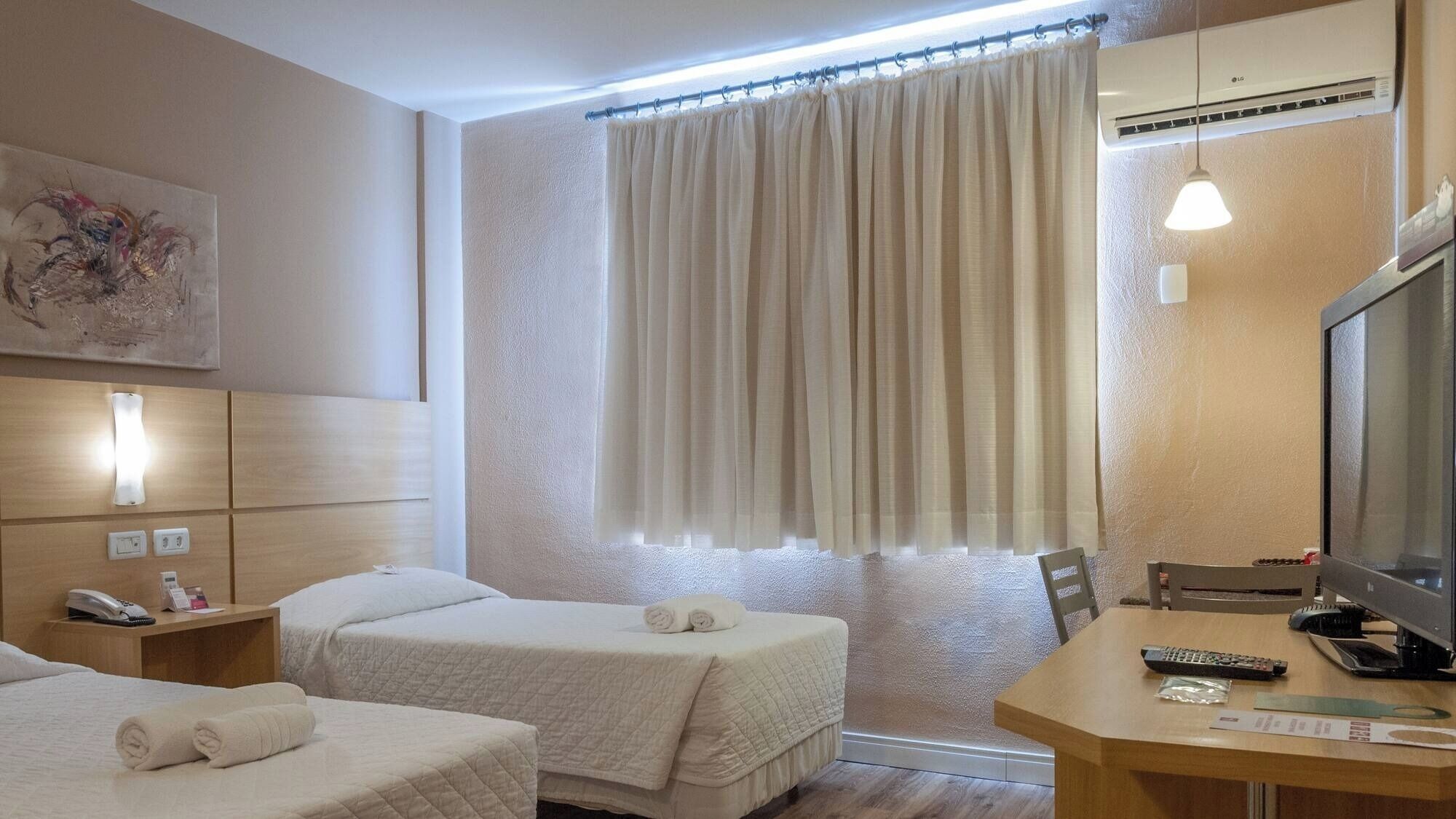Une chambre d’hôtel avec deux lits, un bureau avec un ordinateur, une télévision et un appareil de climatisation.