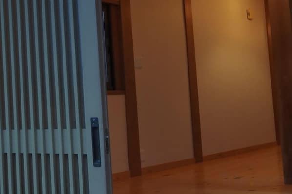 A hallway with a wooden floor, a door with vertical slats, and a wall-mounted light fixture. - Private Japanese-style house for families and groups (Okuma)