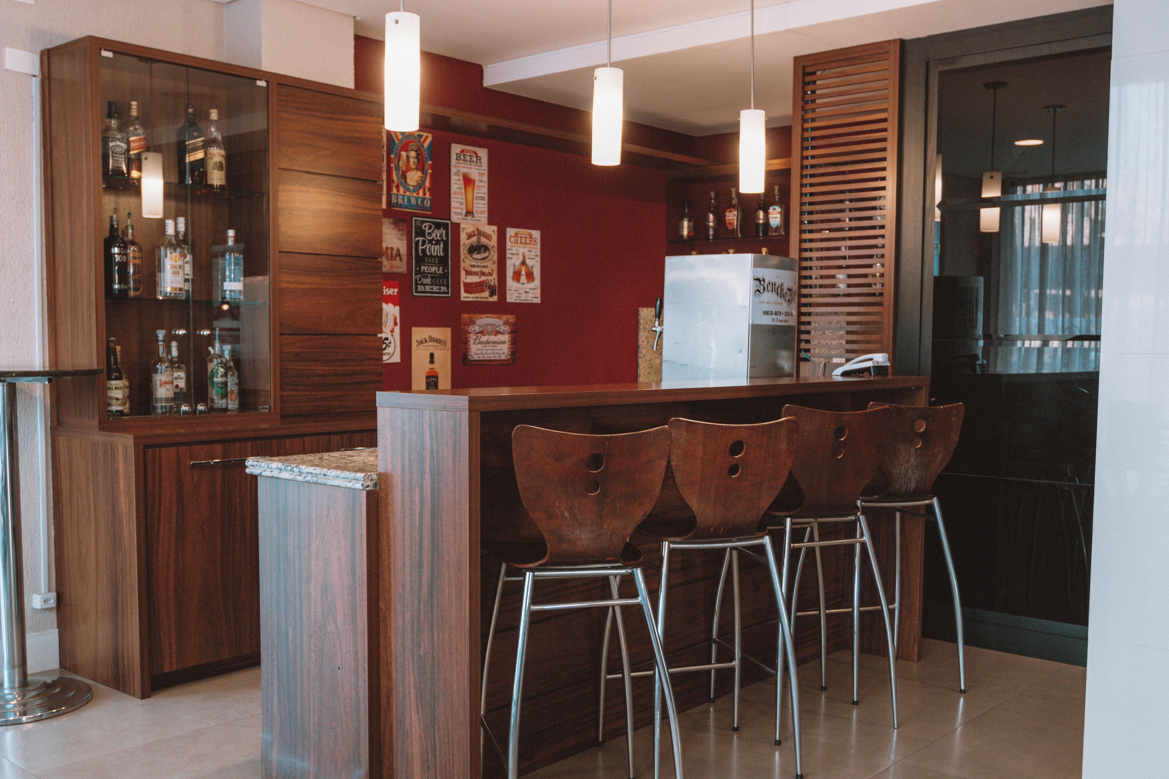 A bar area with wooden cabinets, metal stools, and a refrigerator.