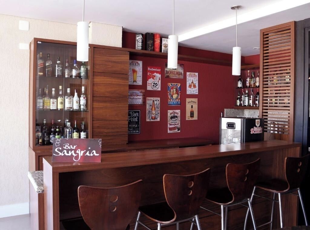 Una zona de bar con mostrador de madera, taburetes y una vitrina con botellas de licor.