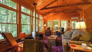 Interior acogedor de una cabaña con ventanas amplias, chimenea, sofá y una mesa de comedor.