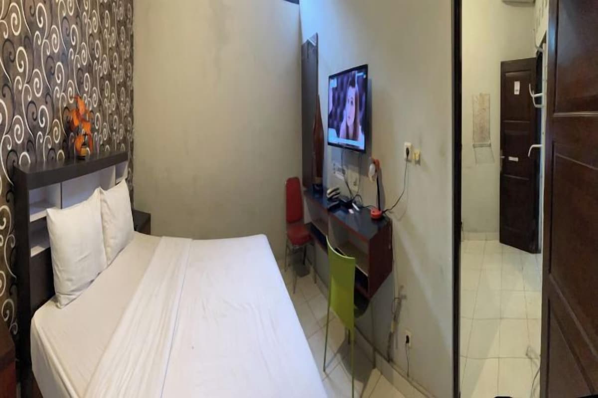A hotel room with a bed, a desk with a computer, a TV, and a mirror.