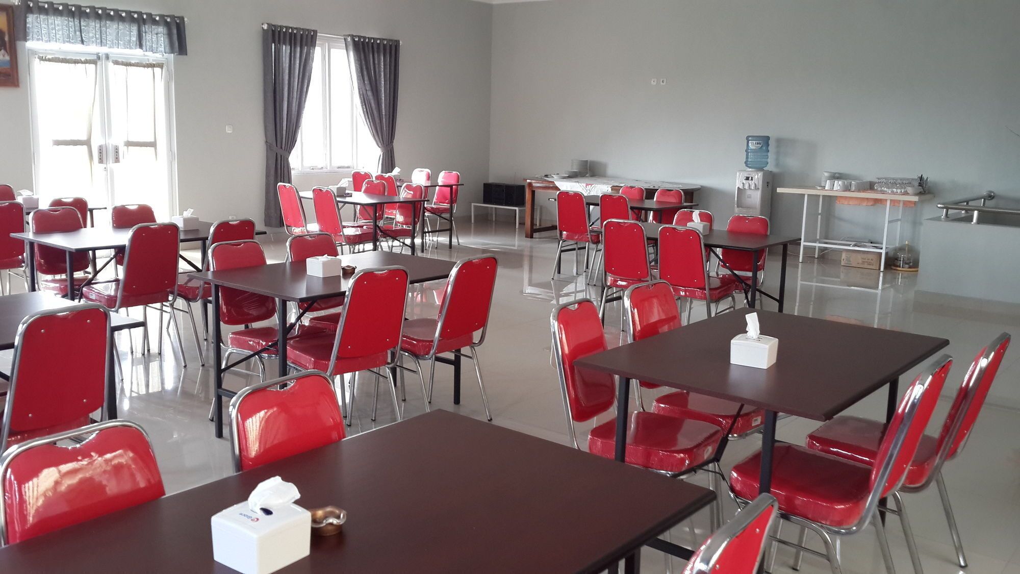 A conference room with multiple tables and chairs, a water dispenser, and a small kitchenette area.