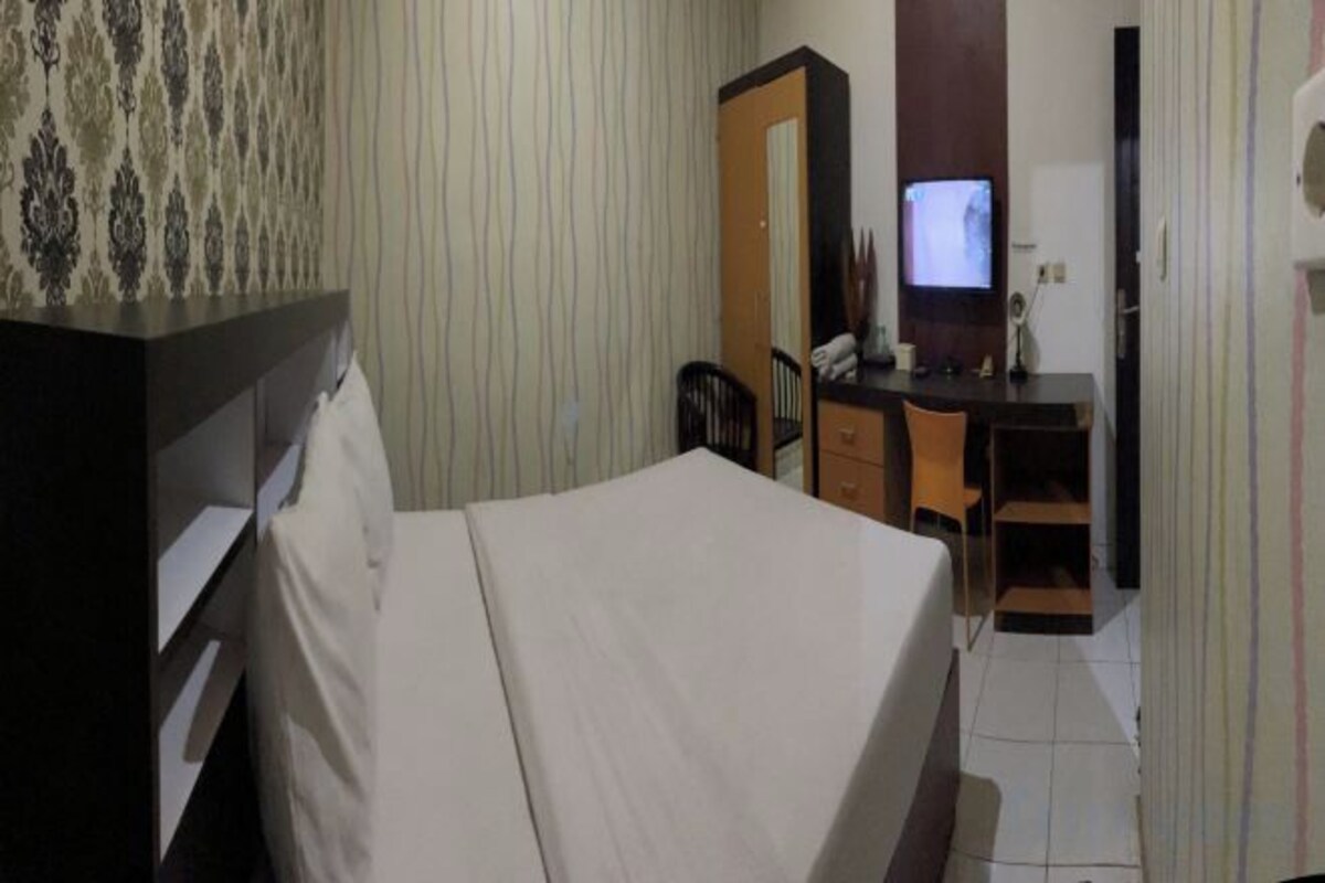 Una habitación de hotel con cama, escritorio, silla, televisor y armario.