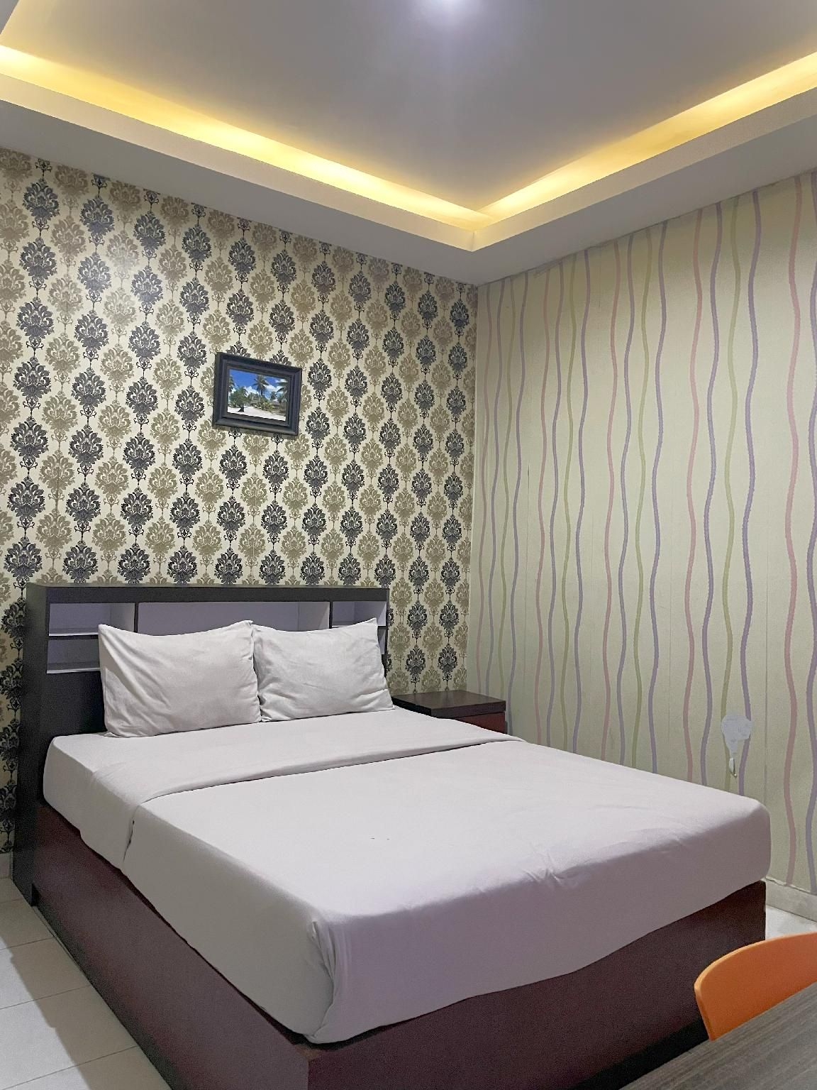 A hotel room with a bed, nightstand, and a picture on the wall.
